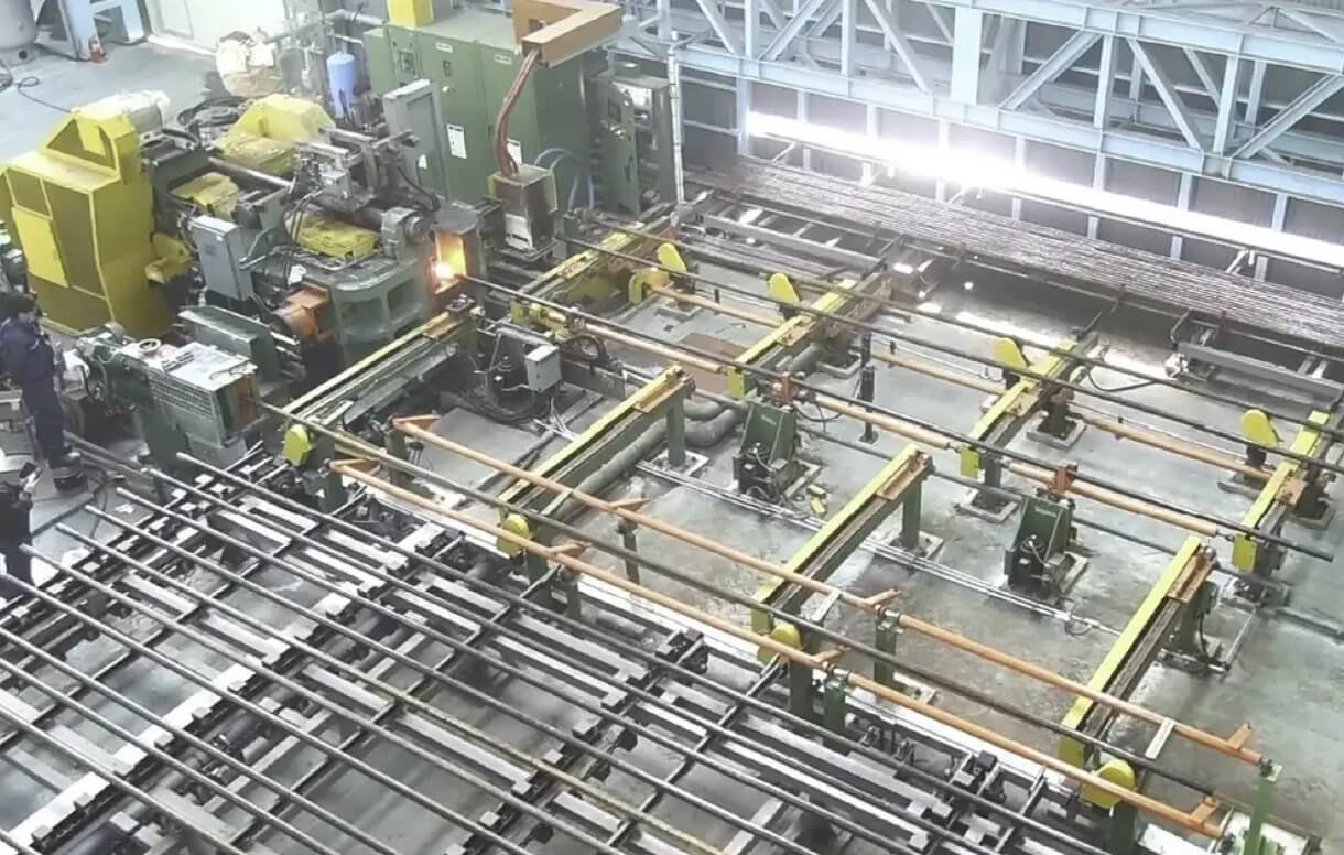 Overhead view of an Ajax forging press automation line with transfer system and heated workpiece in production